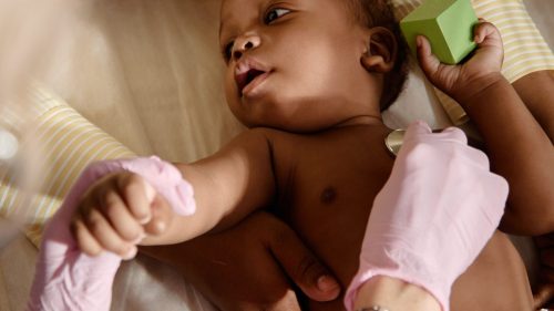Pediatrician using stethoscope on infant held by attentive caregiver, conveying concern and care.