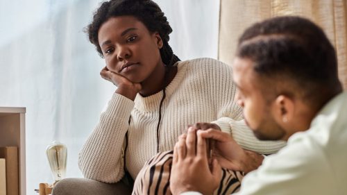 Worried woman consoled by her partner at home, conveying support and empathy.
