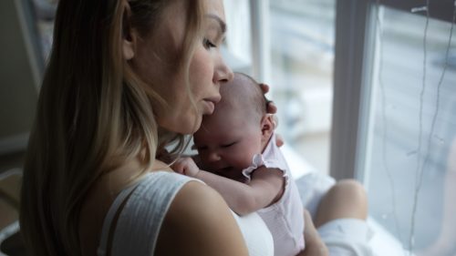 Tender moment of a mother lovingly cradling her infant by a window.
