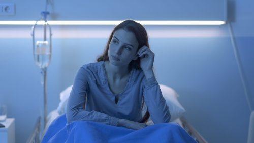 Worried woman sitting in hospital bed at night, contemplating medical outcome.