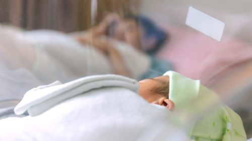 Infant sleeping in hospital, adult resting nearby, conveying concern and care.