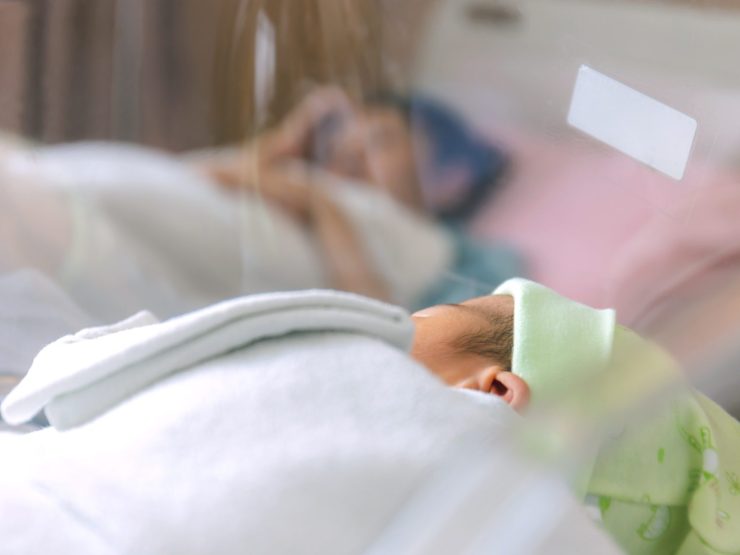 Infant sleeping in hospital, adult resting nearby, conveying concern and care.