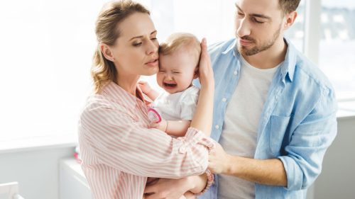 Concerned parents comforting their crying baby, conveying worry and tenderness.