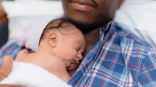Man gently cradles sleeping newborn against chest, conveying warmth and protection.