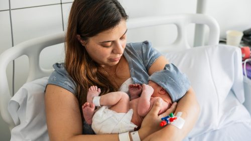 Mother cradling newborn baby in hospital bed, conveying tender care.