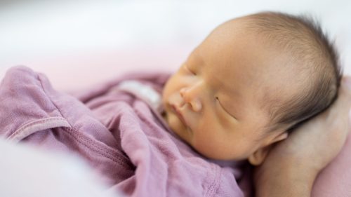 Infant sleeping peacefully in pink swaddling, conveying tenderness and protection.