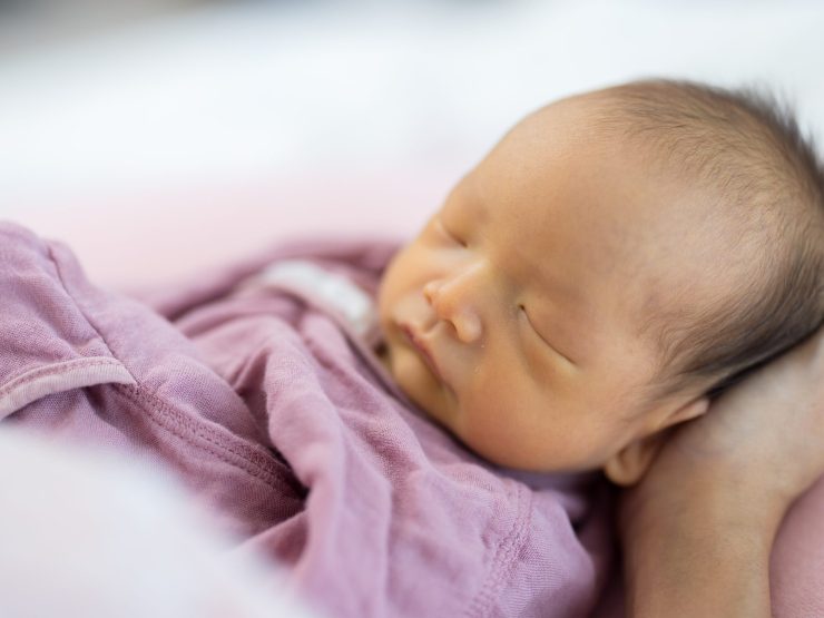Infant sleeping peacefully in pink swaddling, conveying tenderness and protection.