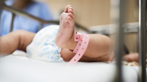 Newborn baby feet with hospital identification bracelet in a medical setting.
