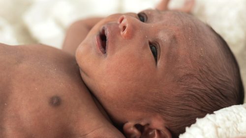 Newborn infant rests on soft white blanket, evoking innocence and vulnerability.