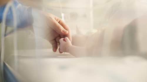 Adult gently holding infant's hand in a caring hospital environment.