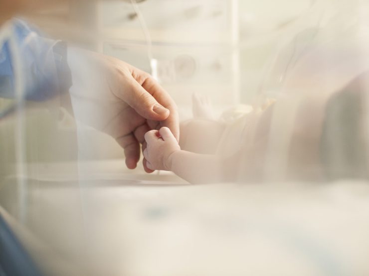 Adult gently holding infant's hand in a caring hospital environment.