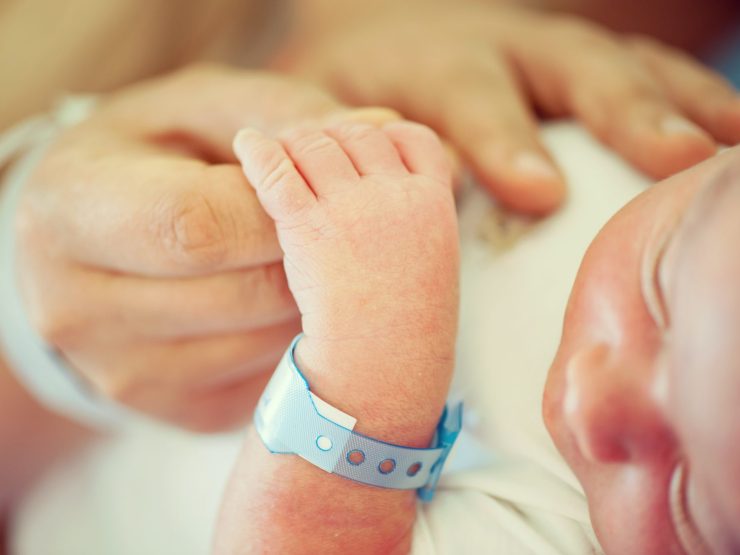Infant's hand grasping adult finger, hospital bracelet visible, evokes vulnerability and care.