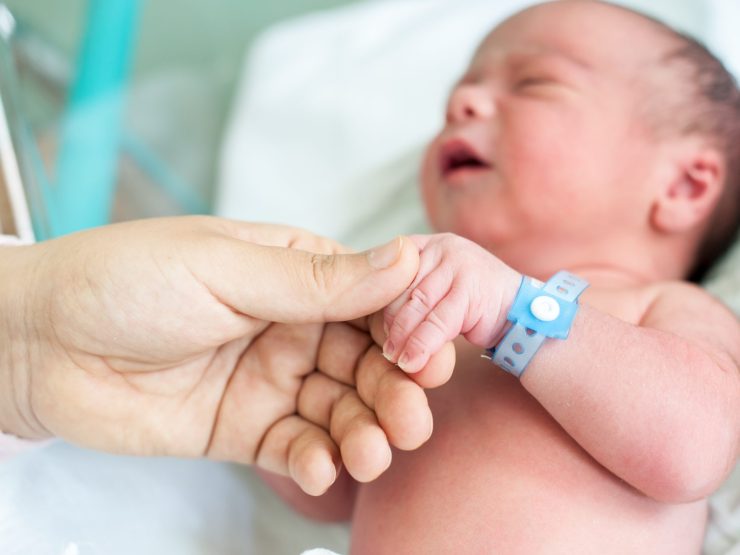 Newborn holding adult's hand in hospital, signifying trust and care.