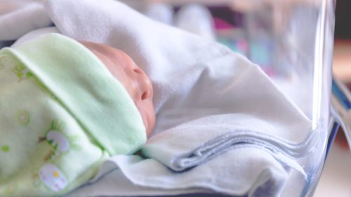 Sleeping infant in hospital bassinet, wrapped in a green blanket, peaceful atmosphere.