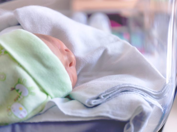 Sleeping infant in hospital bassinet, wrapped in a green blanket, peaceful atmosphere.