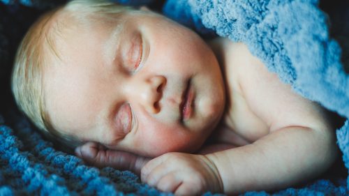 Infant peacefully sleeping, wrapped in a soft blue blanket.