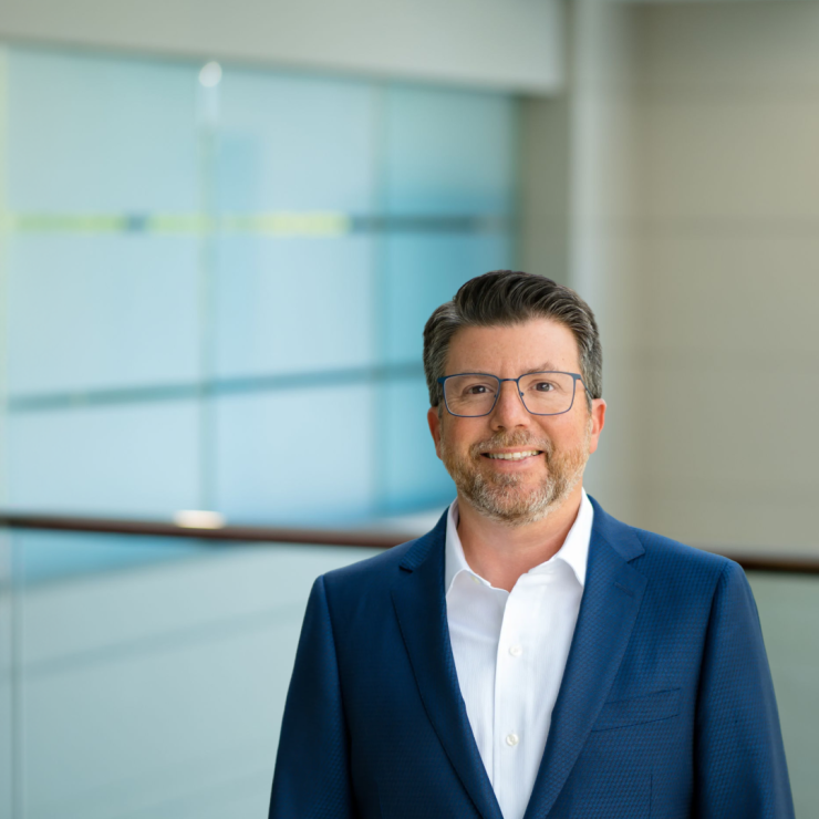 Smiling professional man in suit against modern glass office background.