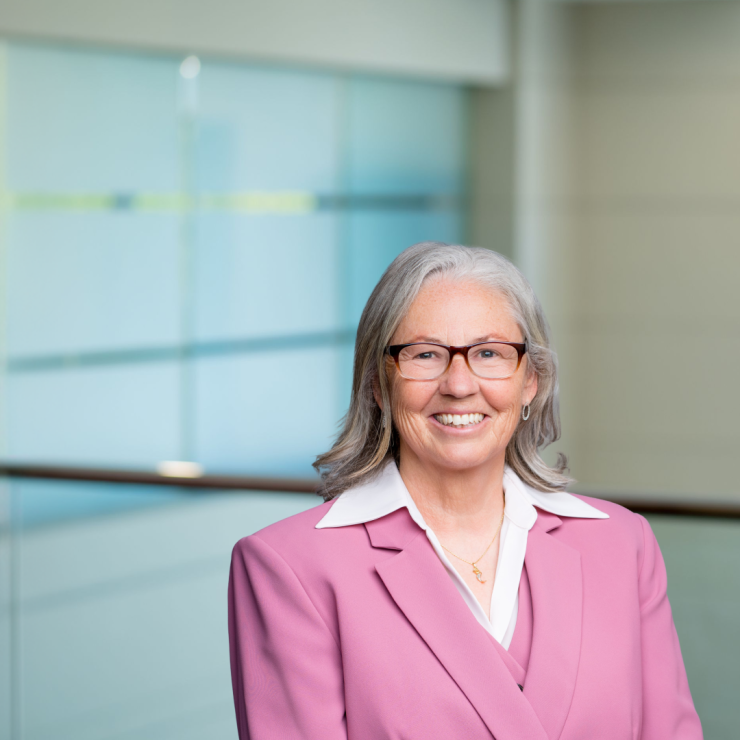 Professional smiling woman in a pink suit in a modern office environment.