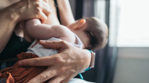 Mother tenderly holding infant by window, conveying warmth and protection.