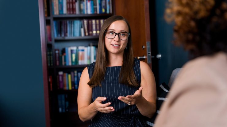 Lawyer discussing case with client in office, bookshelf in background.