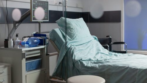 Empty hospital room with bed, medical equipment, and subdued lighting.