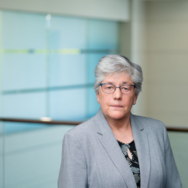 Professional woman in a suit, serious expression, standing in modern office setting.