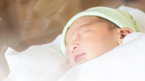 Newborn peacefully sleeping in hospital, swaddled in white blanket.