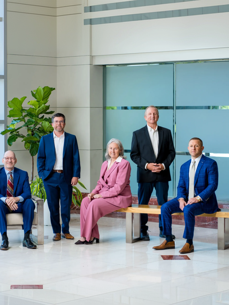 Professional law firm team in formal attire, standing confidently in a modern office lobby.