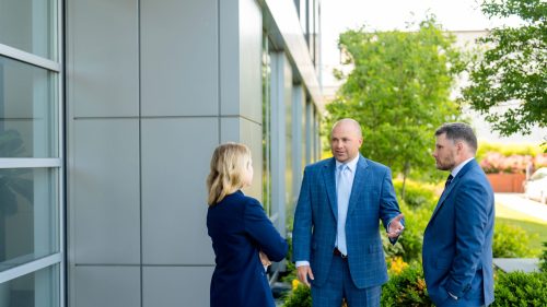 Three professionals in suits discussing outside a modern office building, focused and engaged.