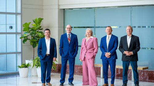 Five lawyers in formal attire standing confidently in a modern office lobby.