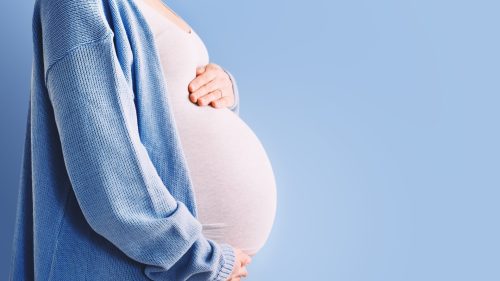 Pregnant woman gently holding her stomach, wearing a blue cardigan.