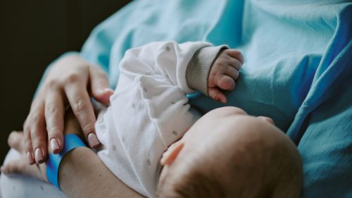Infant cradled in caregiver's arms, conveying trust and vulnerability.