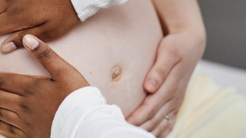 Hands gently supporting an expectant mother's belly, conveying care and empathy.