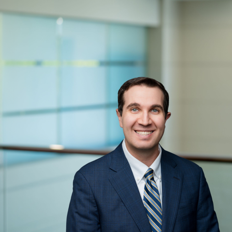 Smiling professional in a suit, standing in a modern office setting.