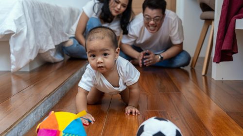 Infant crawling towards colorful toys, with smiling parents watching closely.