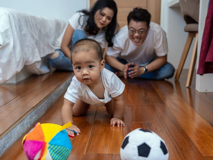 Infant crawling towards colorful toys, with smiling parents watching closely.
