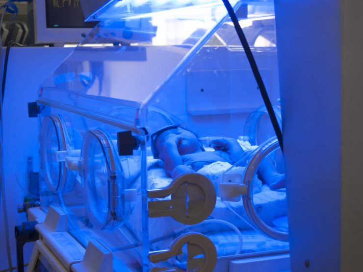 Infant receiving light therapy in hospital incubator, highlighting medical care vulnerability.