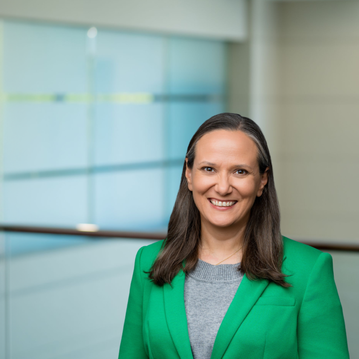 Smiling professional woman in a green blazer in modern office setting.