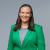 Smiling professional woman in green blazer against neutral background.