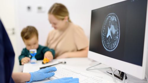 Doctor consulting mother and child in hospital with brain scan displayed.