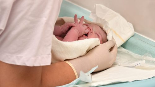 Newborn baby receiving medical care in hospital, health professional observing attentively.