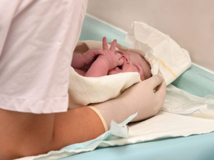 Newborn baby receiving medical care in hospital, health professional observing attentively.