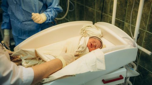 Newborn baby resting peacefully in hospital bed with medical staff attending.