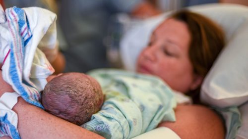 Newborn resting peacefully in mother’s arms, hospital setting, calm and nurturing atmosphere.