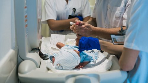 Healthcare team examines newborn in hospital, focused on infant's well-being.