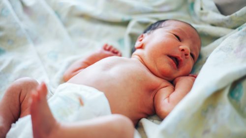 Infant peacefully resting on a soft, patterned blanket in a cozy setting.