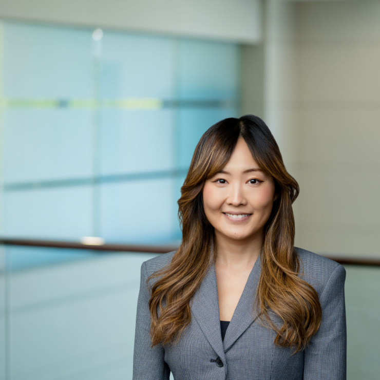 Professional lawyer smiles confidently in modern, glass-walled office setting.