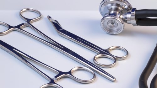 Stethoscope and surgical instruments on white surface, symbolizing medical malpractice issues.