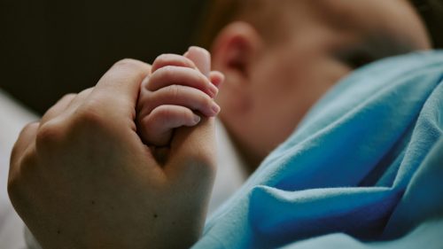 Adult hand gently holding a baby's fingers, symbolizing care and protection.