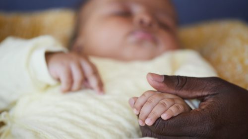 Adult hand gently holding infant's hand, conveying care and protection.